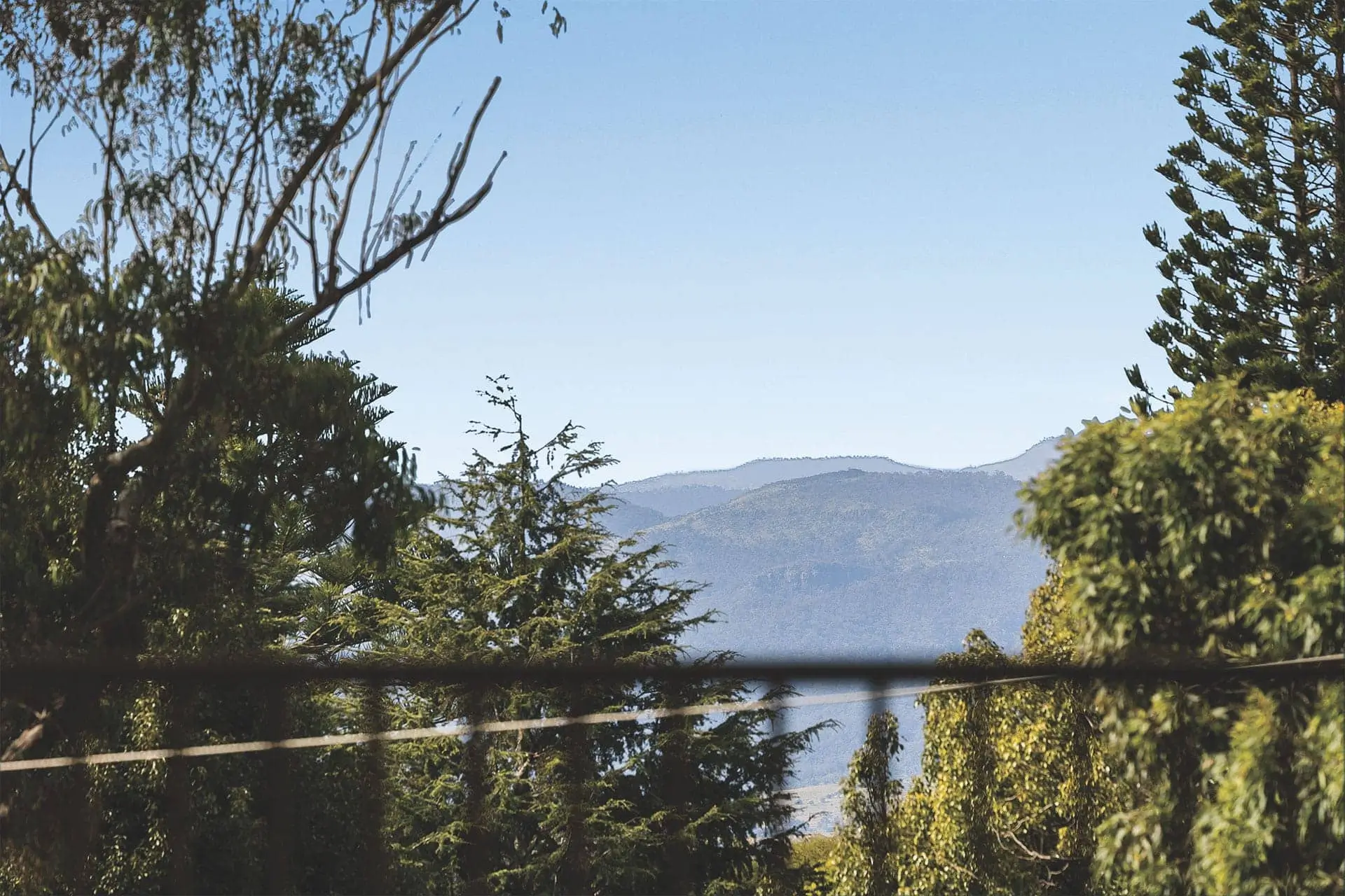 View of distant blue mountains under a clear sky, framed by green trees near a Toowoomba Retirement Community. A thin black wire runs horizontally across the middle of the image.