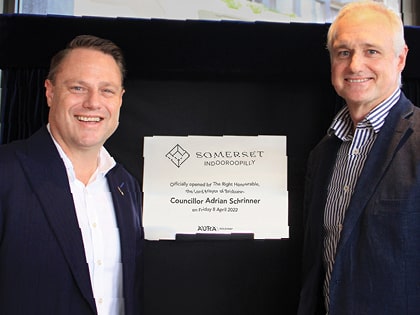 Two men standing beside a plaque that reads "Somerset Indooroopilly, officially opened by Councillor Adrian Schrinner on Friday 6 April 2020." They are smiling and dressed in business attire.