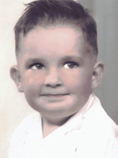 A young child with short, dark hair and wearing a white shirt, smiling slightly while looking off to the side. The photo has a classic black and white style.