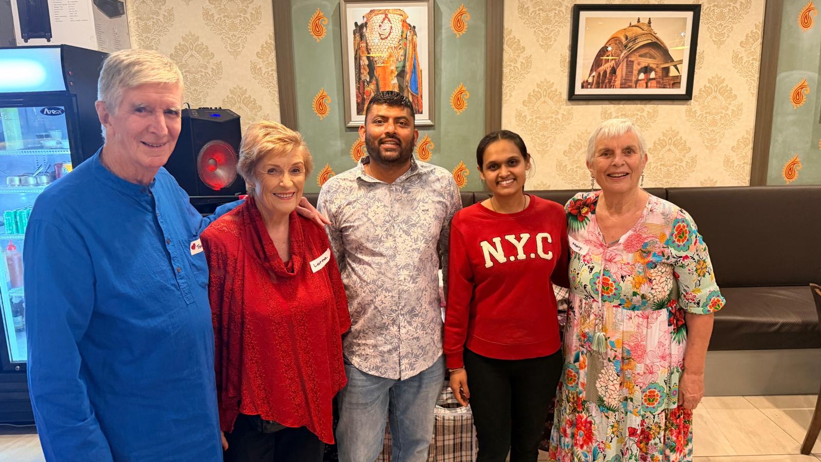 Five people stand closely together and smile for the camera in a warmly lit room with patterned wallpaper and framed pictures, celebrating an award-winning Somerset gathering.